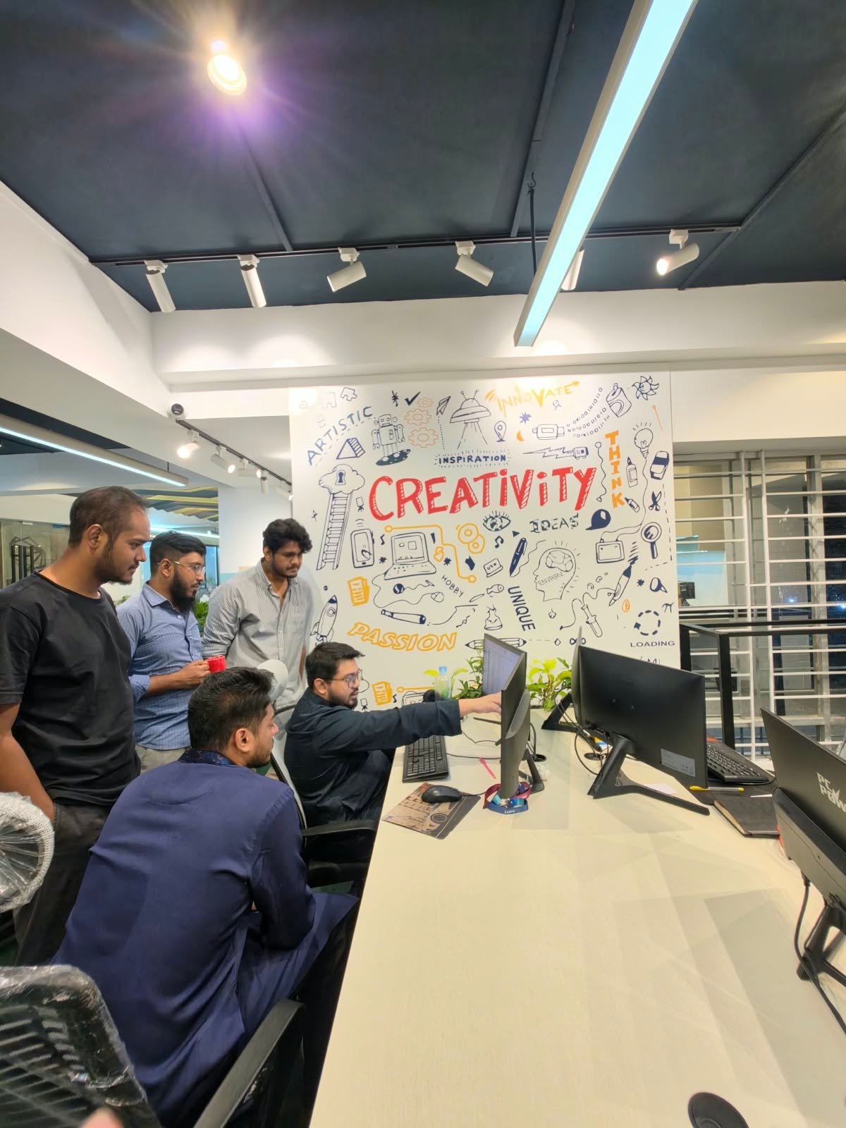 IMPIT team gathered around a workstation reviewing work together beside the Creativity wall